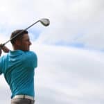 Young golfer driving with a wood against cloudy skies