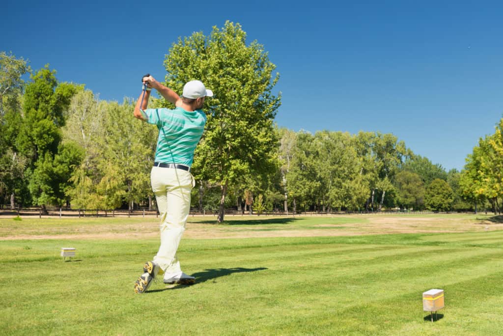 Golfer teeing off with iron club. Golf ball visible in the upper right corner.