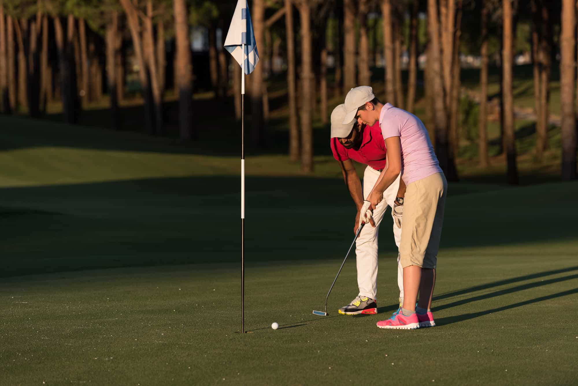 male golf instructor teaching female golf player, personal trainer giving lesson on golf course