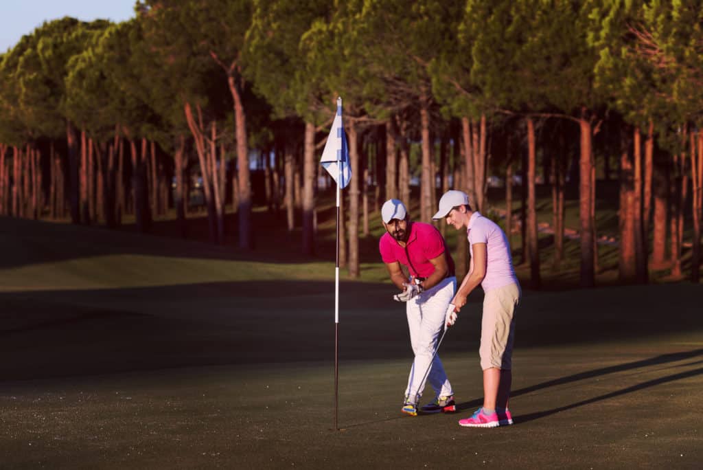 male golf instructor teaching female golf player, personal trainer giving lesson on golf course