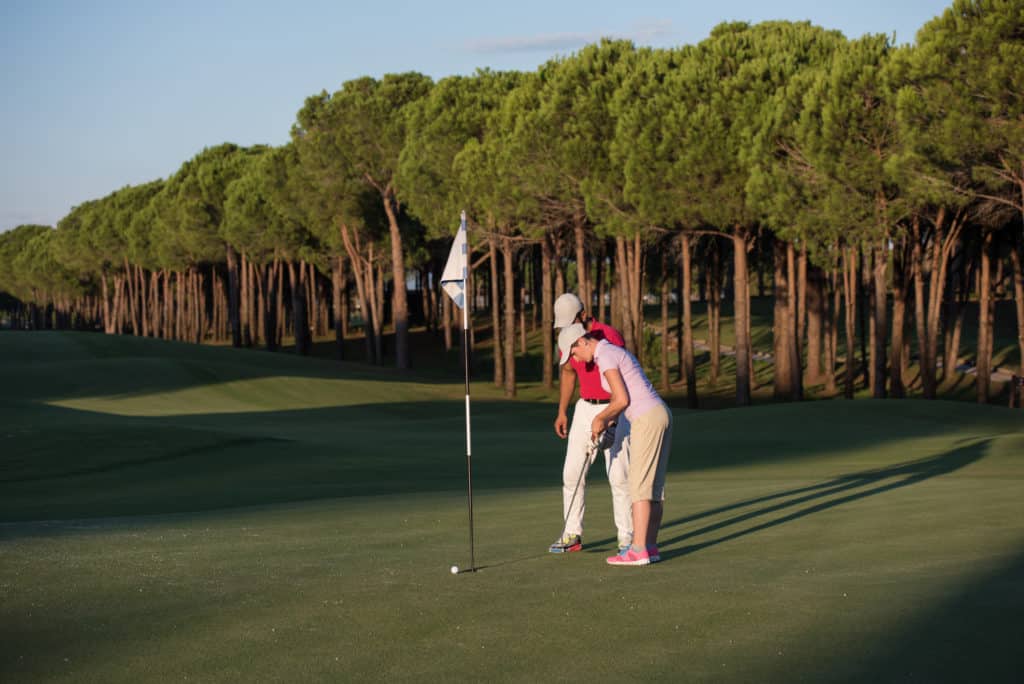 male golf instructor teaching female golf player, personal trainer giving lesson on golf course