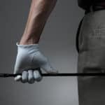 Closeup of a male golfer holding a six iron behind his body. Man has a Golf Glove on his hand. Horizontal format over a light to dark gray background.