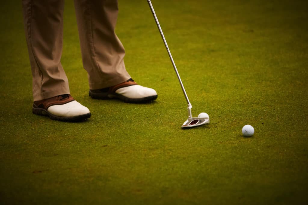 Golf player's legs, two golf balls and golf iron.