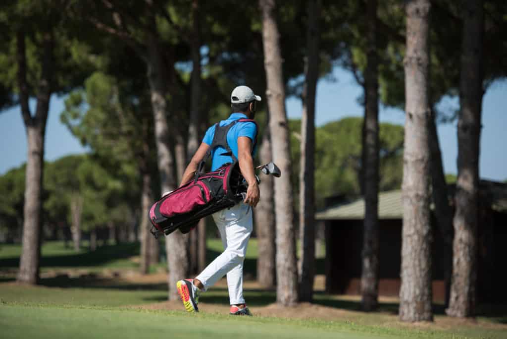 golf player carrying bag and walking at course to next hole