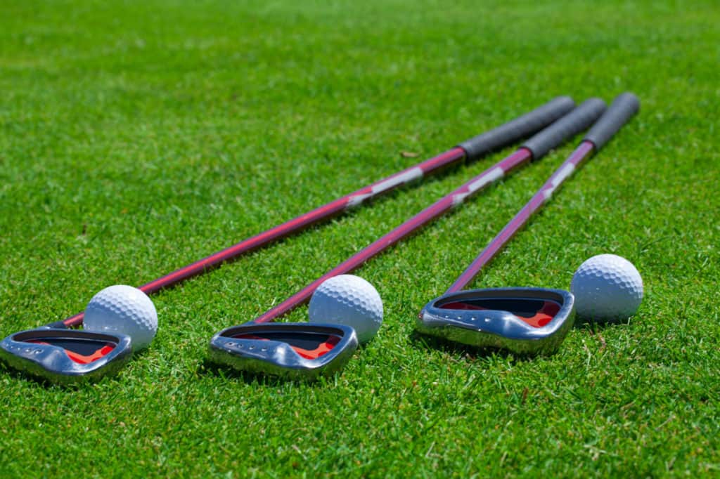 A golf ball rests on the tee grass with irons. Selective focus with plenty of copy space.