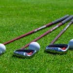 A golf ball rests on the tee grass with irons. Selective focus with plenty of copy space.