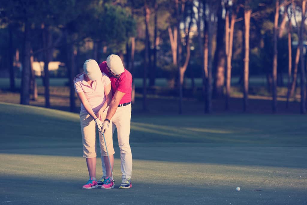 male golf instructor teaching female golf player, personal trainer giving lesson on golf course