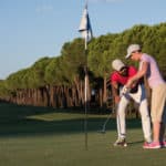 male golf instructor teaching female golf player, personal trainer giving lesson on golf course