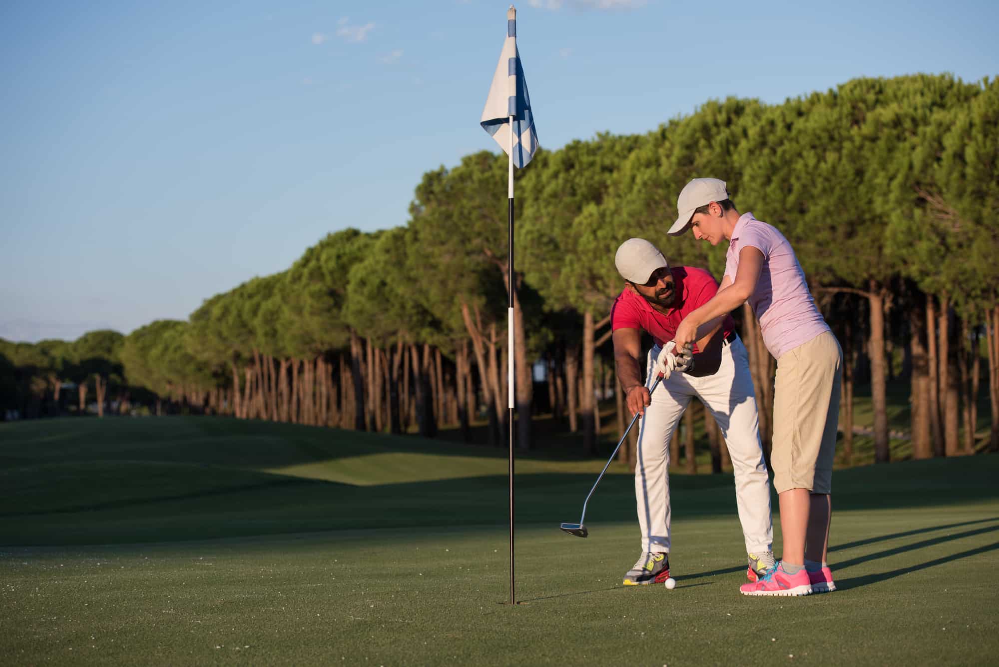 male golf instructor teaching female golf player, personal trainer giving lesson on golf course