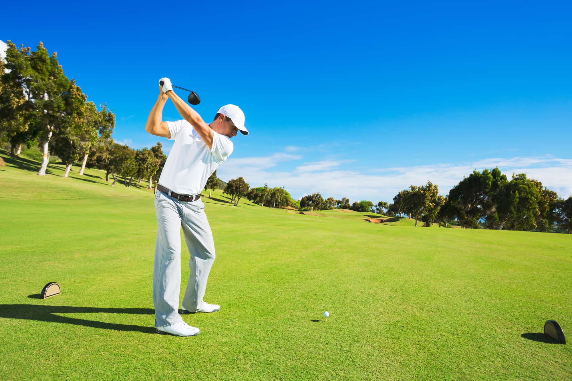 Golf player teeing off. Man hitting golf ball from tee box with driver.