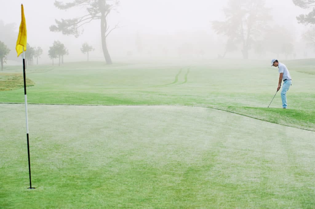 Golfer chipping onto the green at sunrise on the golf course in misty conditions