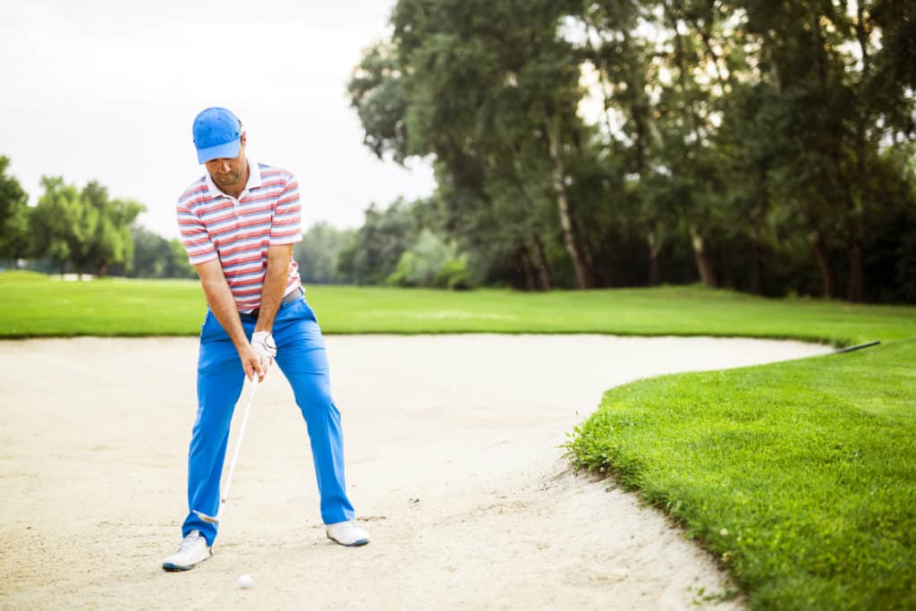 Golfer taking a bunker shot with the ball being in sand