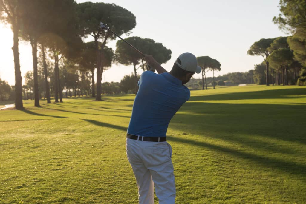 handsome sporty man, golf player hitting shot with club on course at beautiful morning