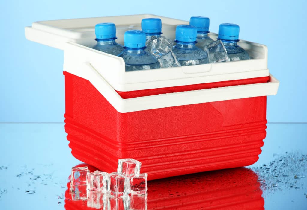 Traveling refrigerator with bottles of water and ice cubes, on blue background