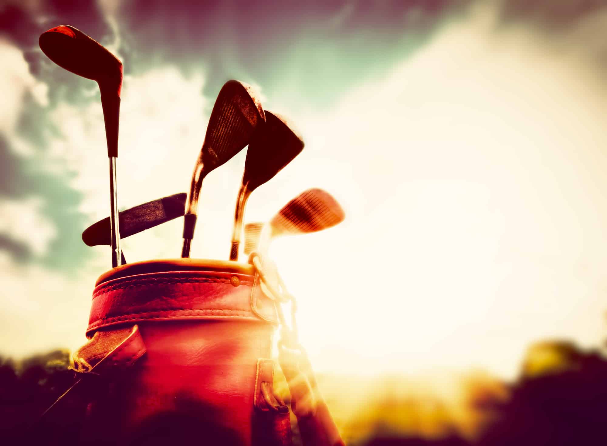 Golf clubs in a leather baggage in vintage, retro style at sunset