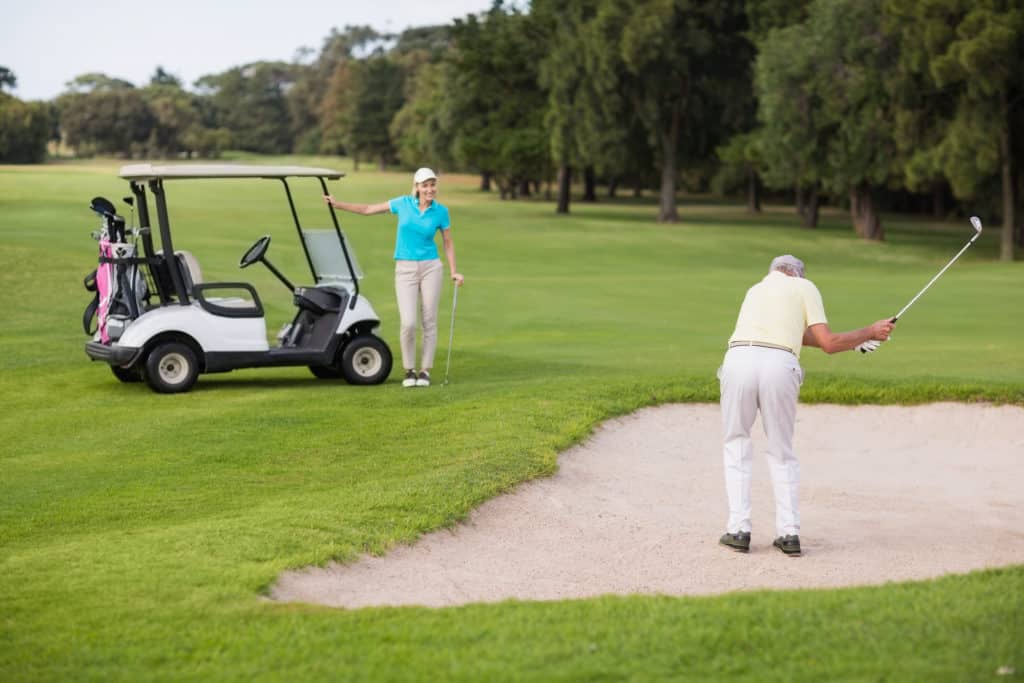 Mature golfer standing on sand trap by woman at golf course