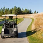 A golf cart on a path going through a golf course with a sign to keep carts on path at lower right.