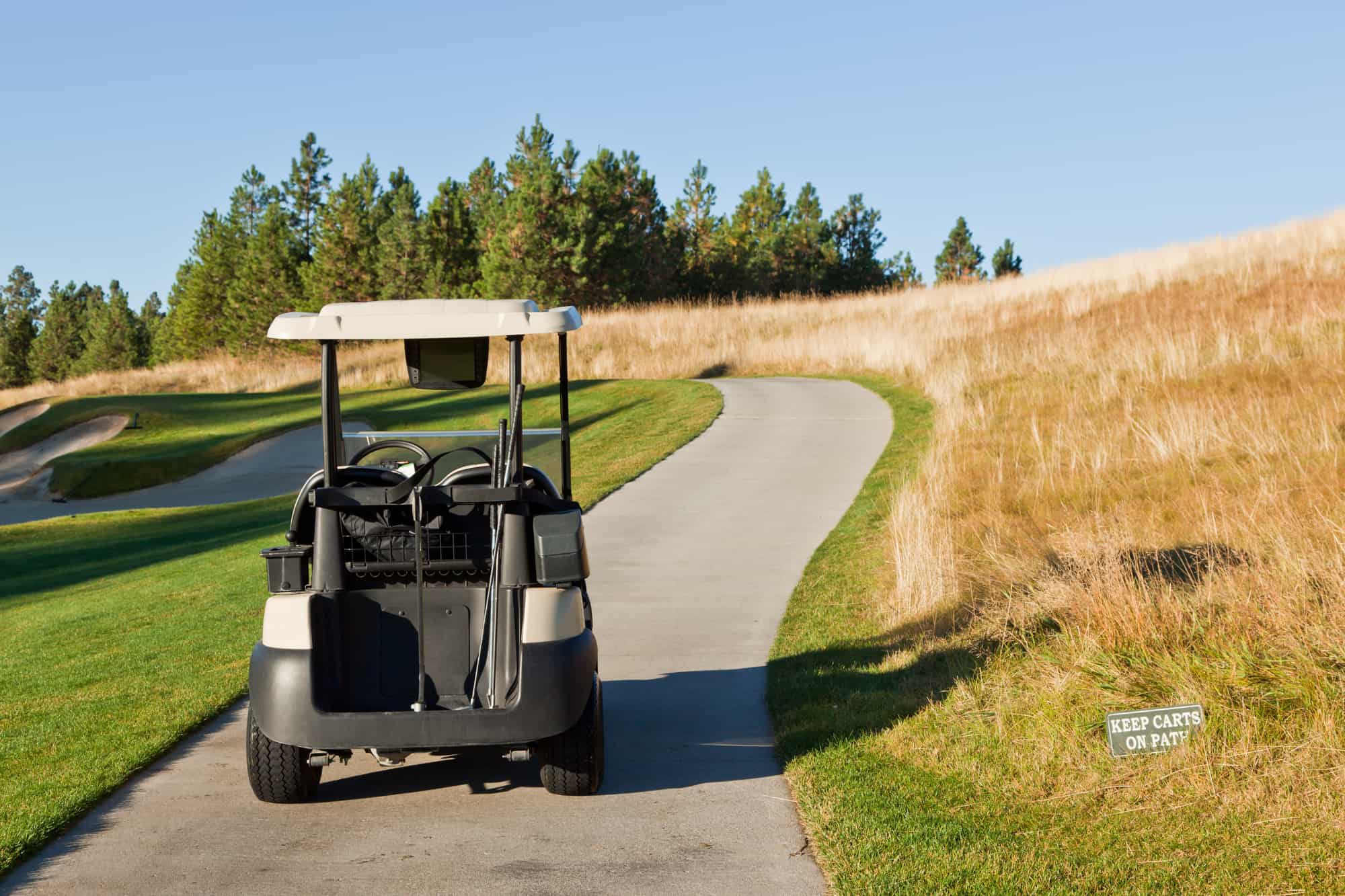 A golf cart on a path going through a golf course with a sign to keep carts on path at lower right.