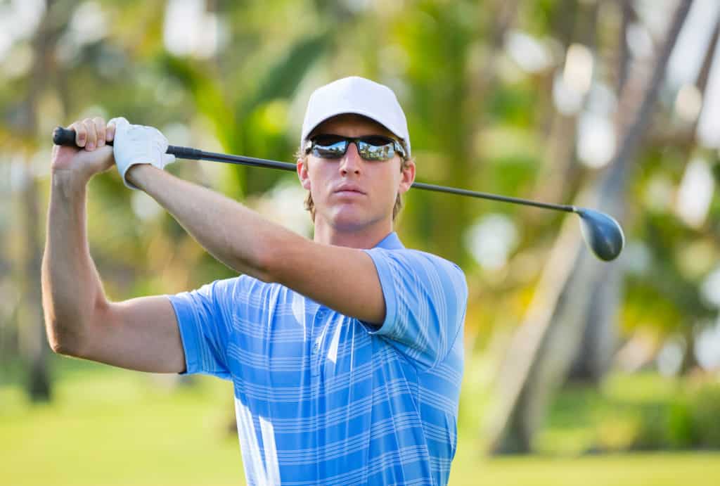 Athletic young man playing golf, golfer hitting fairway shot, swinging club