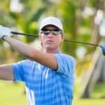 Athletic young man playing golf, golfer hitting fairway shot, swinging club