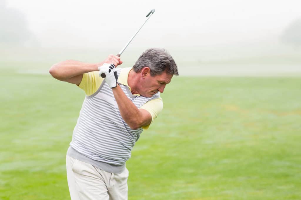 Golfer swinging his club on the course on a foggy day at the golf course