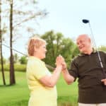 One team. Smiling senior man and woman standing on course holding golf clubs and their hands together
