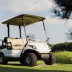View from low angle, white golf cart stands on a stone walkway against a background of grass and trees