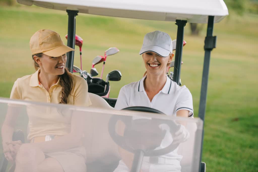 Smiling female golf players riding golf cart at golf course