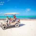 Little girls and mother driving golf cart at tropical beach