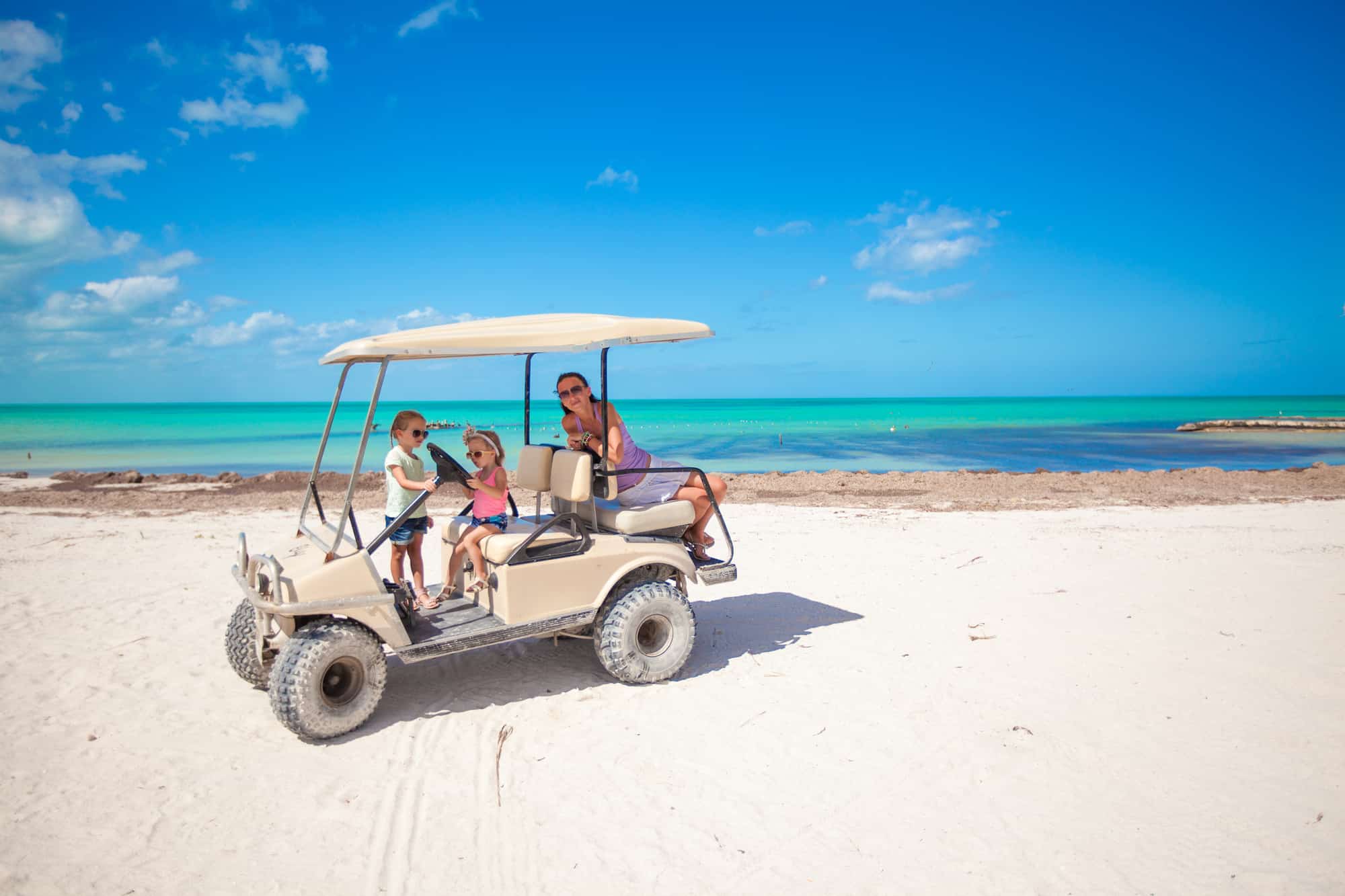 Little girls and mother driving golf cart at tropical beach