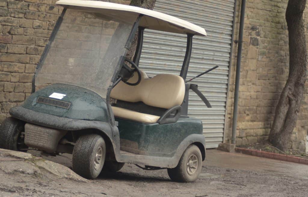 Old and dirty golf cart parked near the garage