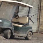 Old and dirty golf cart parked near the garage