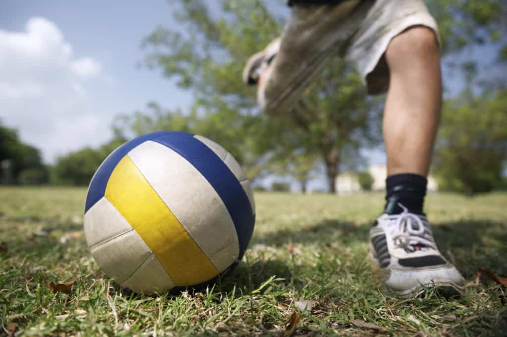 Kids playing soccer game, young boy hitting ball in park