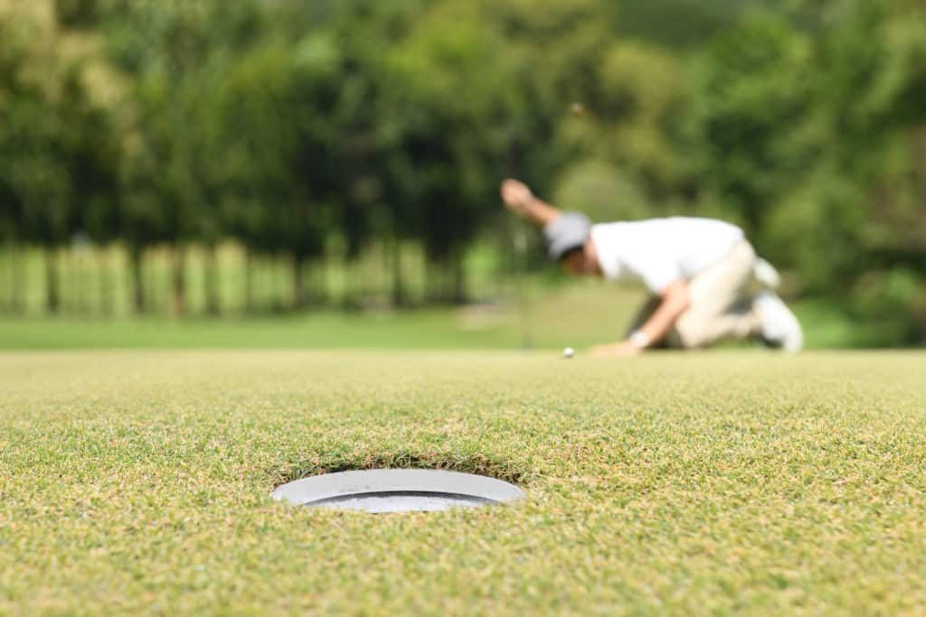 Man golfer check line for putting golf ball on green grass