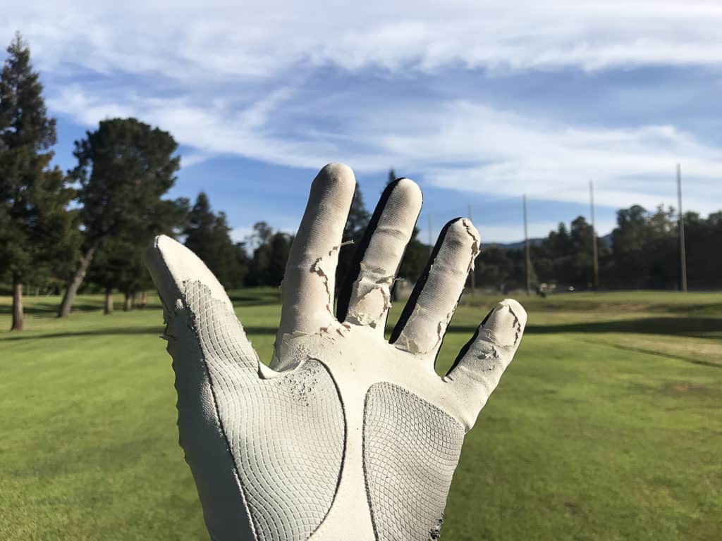 Old weathered white golf glove on the raised and open left hand. Blurred golf course with beautiful sky