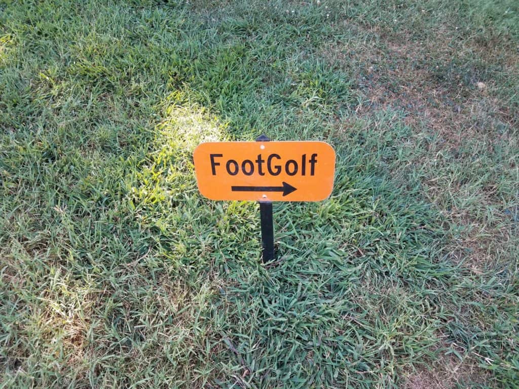 orange foot golf sign with black arrow in grass