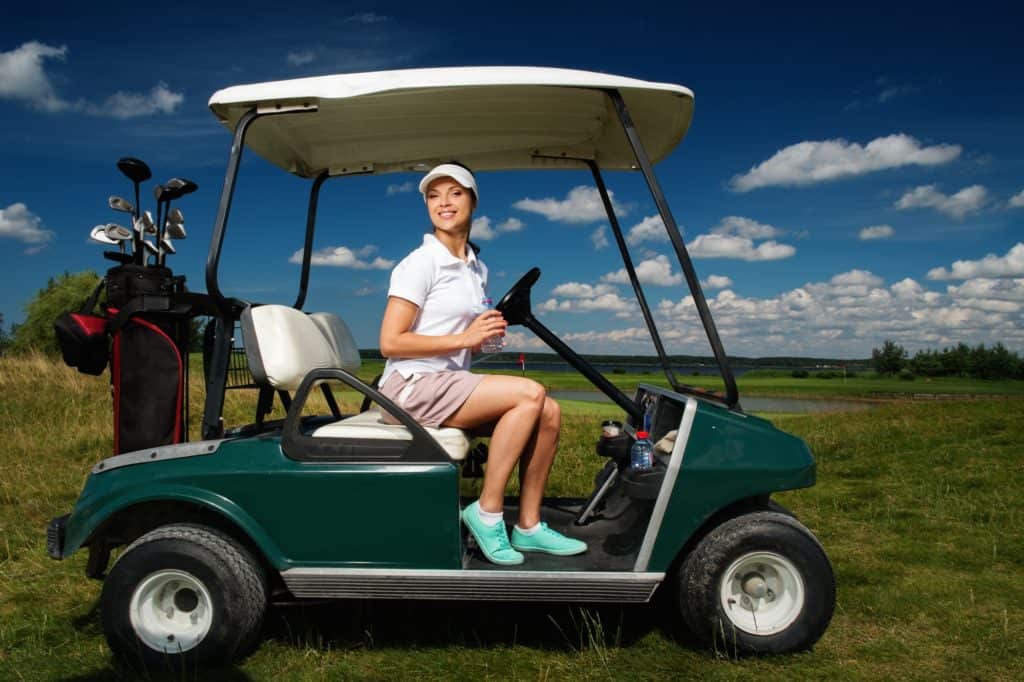 Young cheerful woman driving golf cart