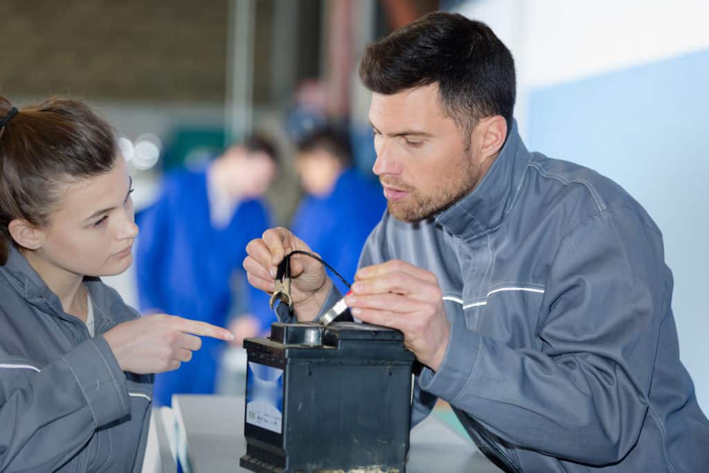 mechanic with apprentice attaching cables to battery