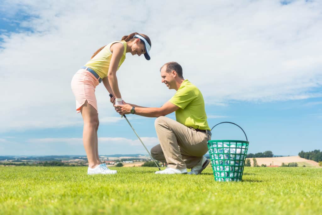 Young woman exercising the golf swing helped by her instructor