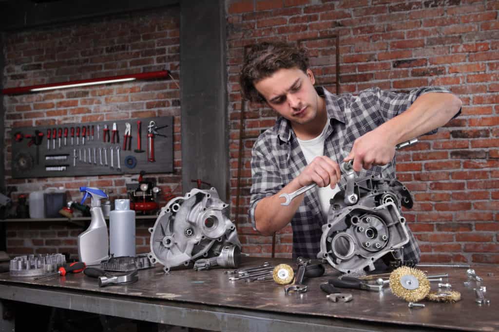 man work with the wrench, repair and cleaning engine parts on the workbench in home garage workshop, diy concept