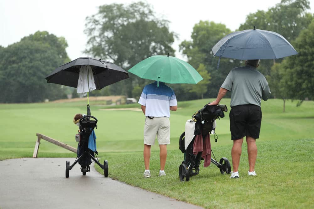 Golfers use umbrellas during a rainy round of golf