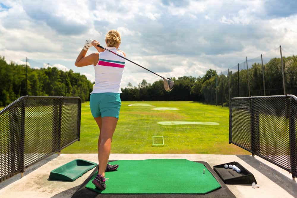 Young woman practices her golf swing on driving range