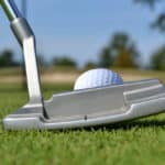 close of putter and golf ball on green
