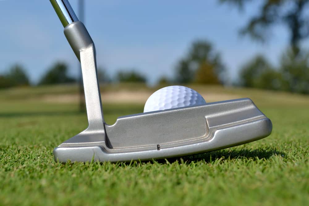 close of putter and golf ball on green