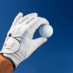 hand wearing golf glove holding a white golf ball