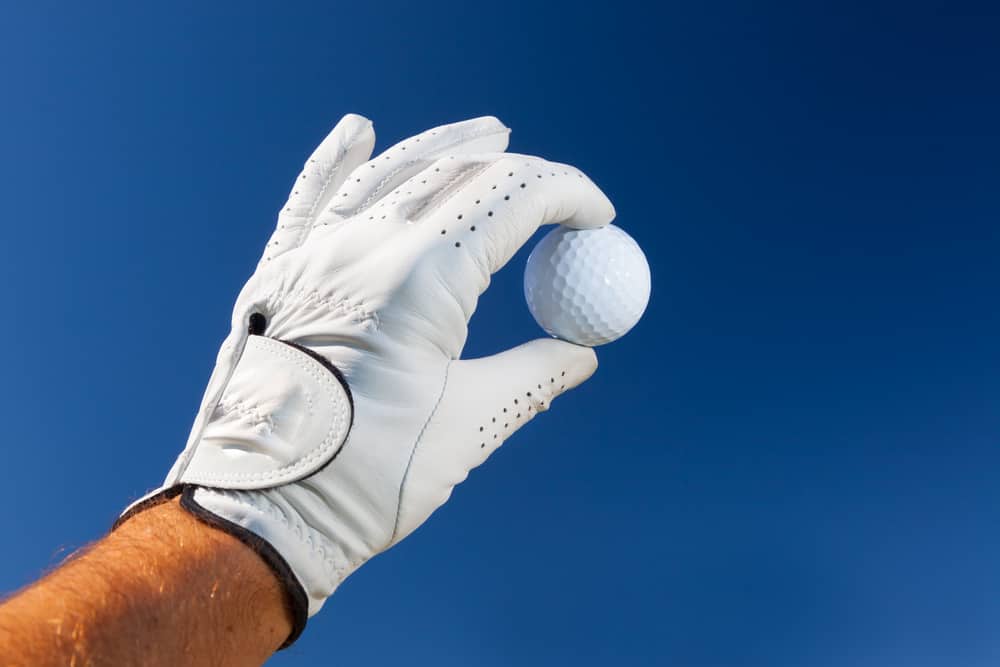 hand wearing golf glove holding a white golf ball