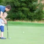 handsome young father teaching his cute son to play golf