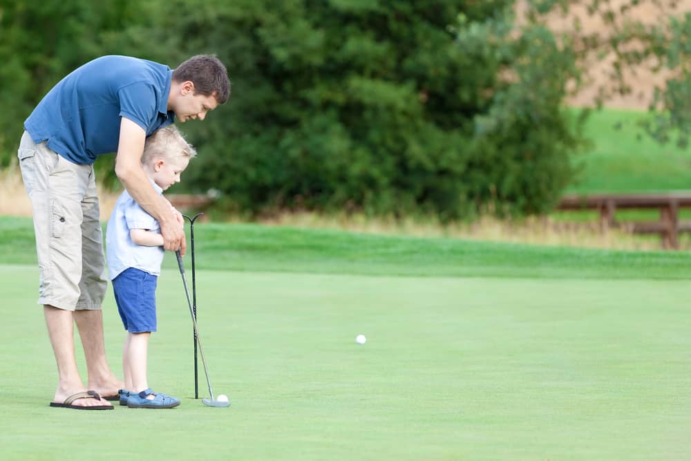 handsome young father teaching his cute son to play golf