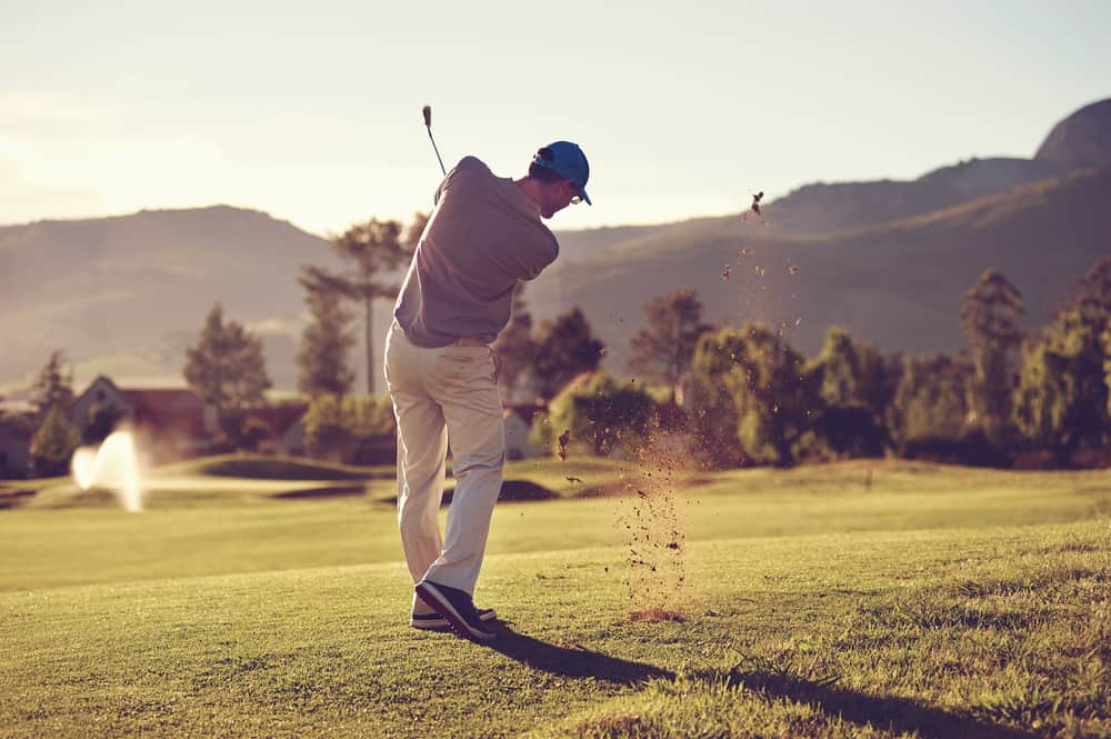 Golfer hitting golf shot with club on course