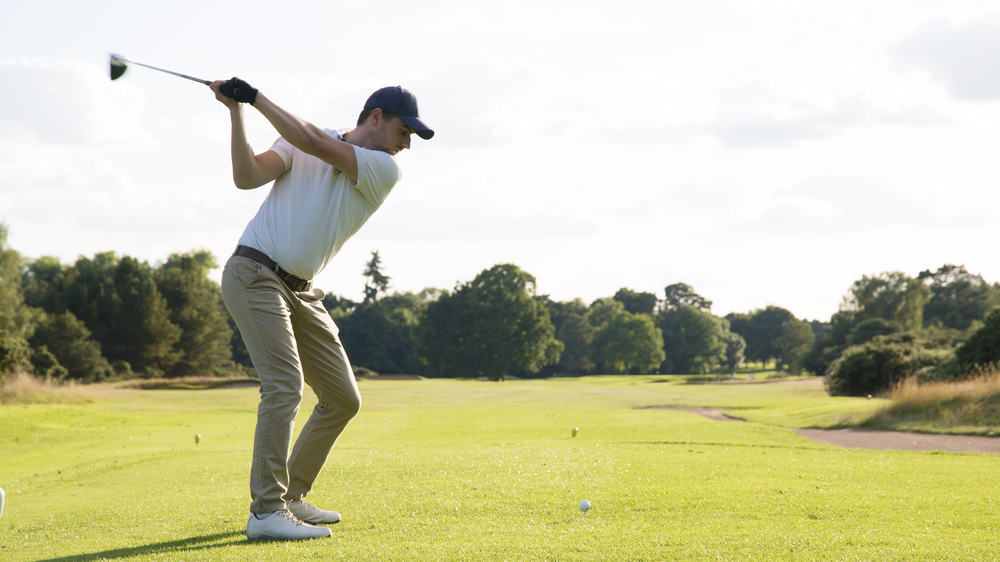 Man hitting driver on a golf course in the sun